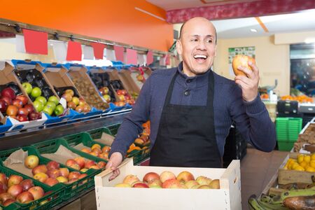 friendly mature male vendor posing with apples in grocery storeの写真素材