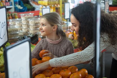 Brunette female with blonde little girl considering mandarins at storeの写真素材