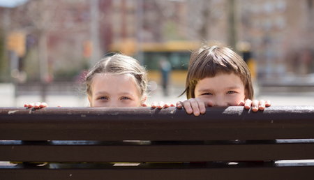 boy with blonde girl hiding on a street bench in autumnの写真素材