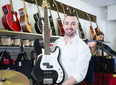 Positive male buyer choosing guitar in music shopの写真素材