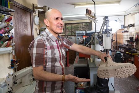 senior Professional shoemaker stitching footwear on machine in shoe atelier