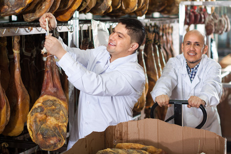 Butchery technologists in white gown checking joints of iberico jamon at factory