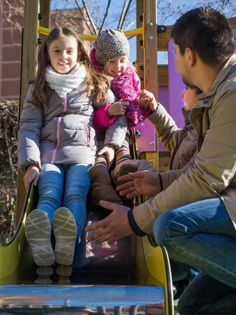Happy parents with two little daughters spend time at playgroundの写真素材