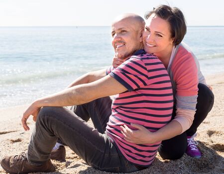 happy couple of mature man and female sitting near sea at sunny day