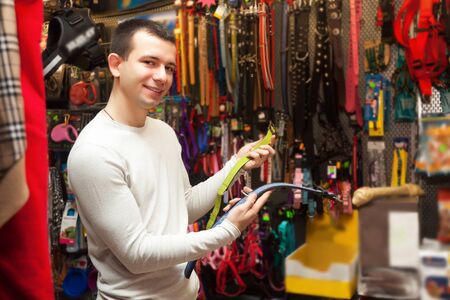 Young man watching dog leads and smiling in zoo shopの写真素材