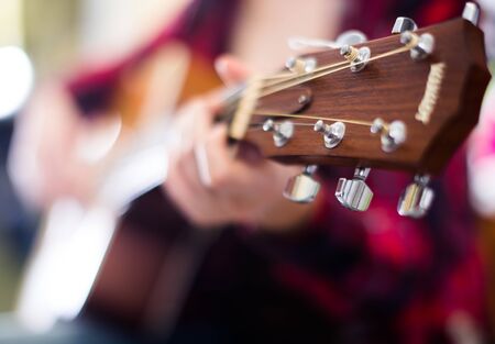 girl is playing acoustic guitar in music shop. Focus on the head of guitar
