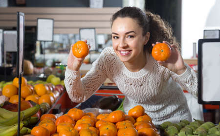 portret of young happy female choosing mandarins at storeの写真素材