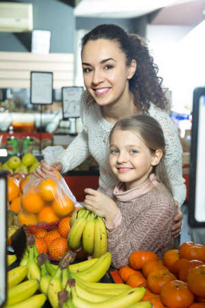 Brunette mother and blonde daughter buying mandarins in shopの写真素材