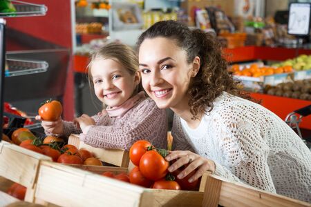 smiling Brunette female with a little girl considering tomatoes at storeの写真素材