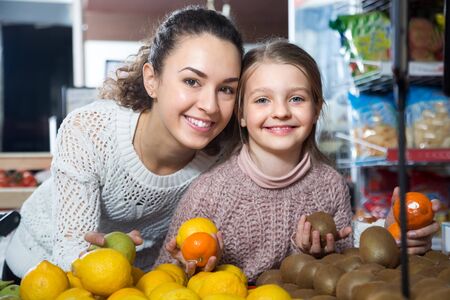 Brunette female with a little girl considering fruit at storeの写真素材
