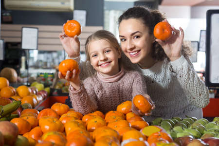 portret of blonde girl with mother buying mandarins in shopの写真素材