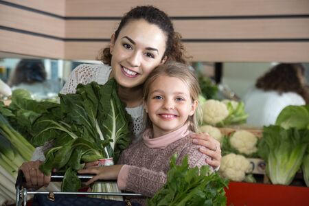 smiling mother and blonde daughter buying greenery in shopの写真素材