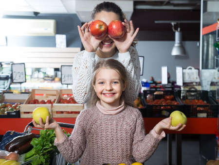 positive woman and lsmiling ittle girl posing whith apples in department fruits of storeの写真素材