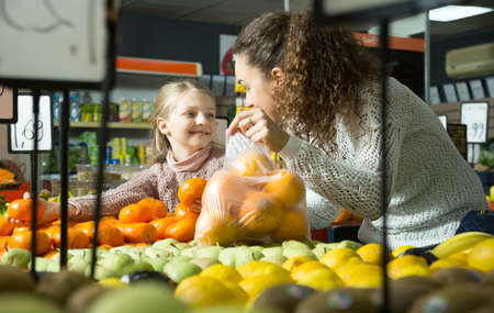 smiling blonde girl with mother buying mandarins in shopの写真素材