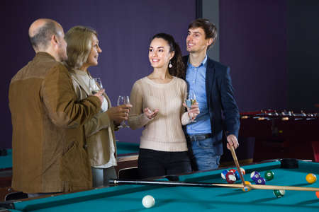 two pairs of different ages, talking with glasses of wine in a billiard hallの写真素材