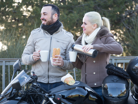 Young woman and man posing near motor bike with sandwitches and coffeeの写真素材