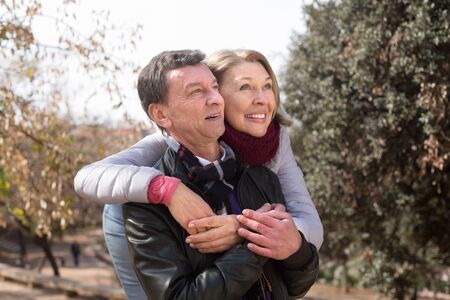 Mature family couple cuddling at park at fall day and smilingの写真素材