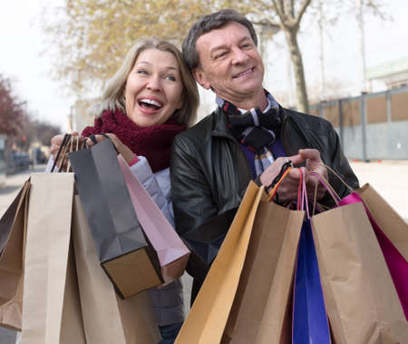 Smiling elderly husband and wife spouses with shopping bags in autumnn dayの写真素材