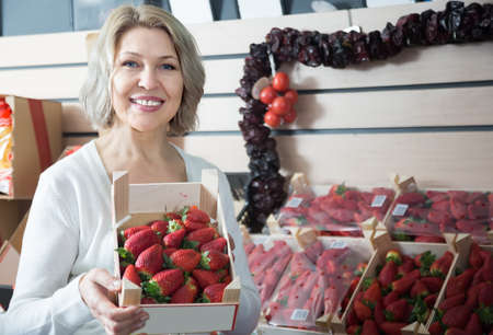female grocery worker selling fresh strawberry at local marketの写真素材