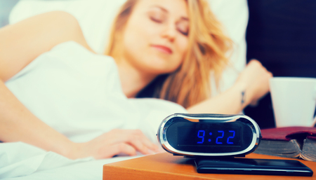woman sleeping near clock and book in bedroomの写真素材