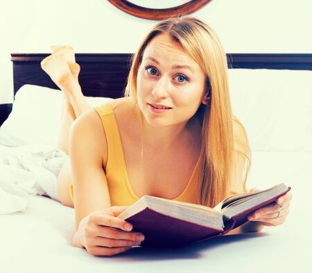 Blonde girl reading book on bedの写真素材