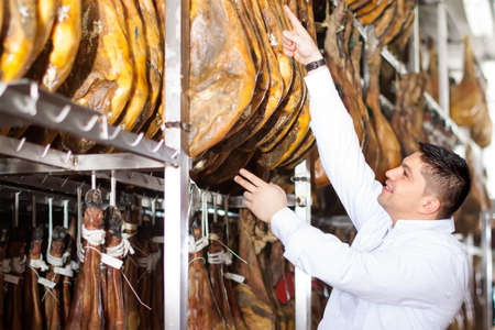 friendly mature butcher posing with jamon joints at meat factoryの写真素材