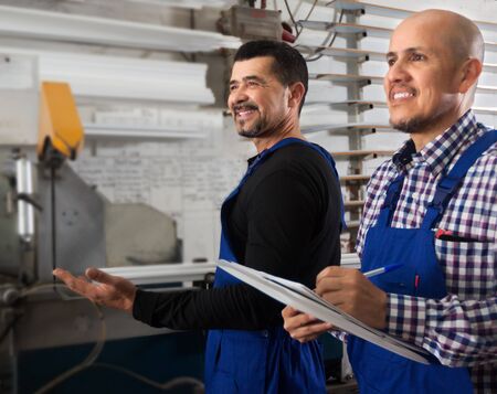 Smiling worker operating in lathe, his boss with papers nearbyの写真素材