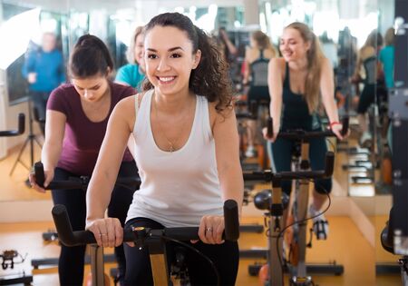 shapely females riding stationary bicycles in modern gym for womenの写真素材