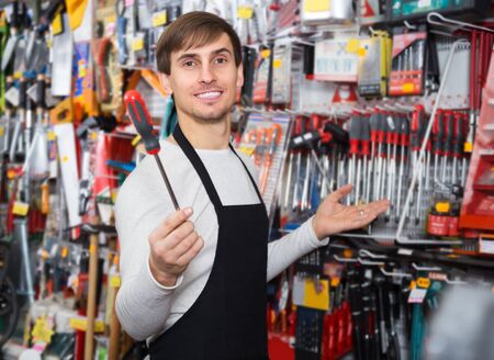 Young male seller posing at tooling section of household storeの写真素材