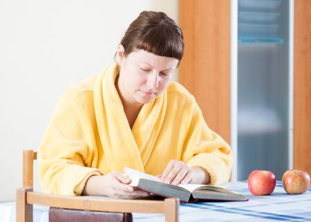 Woman reading a book in a yellow bathrobe at homeの写真素材