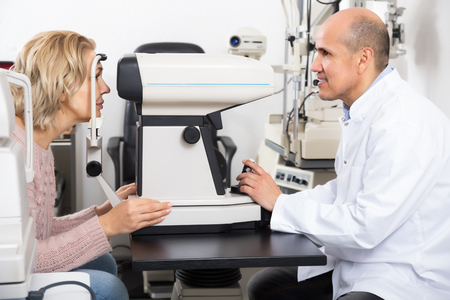 Mature male ophthalmologist and female pensioner checking eyesight in clinicの写真素材