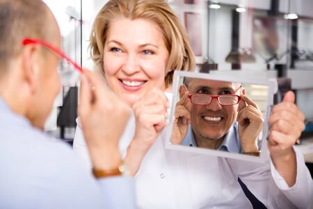 charming  female optician consulting mature male customer about framesの写真素材