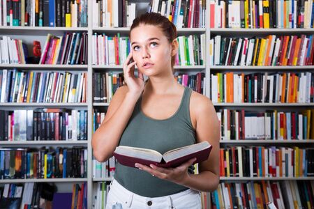 perplexed brunete girl chooses a book in the libraryの写真素材