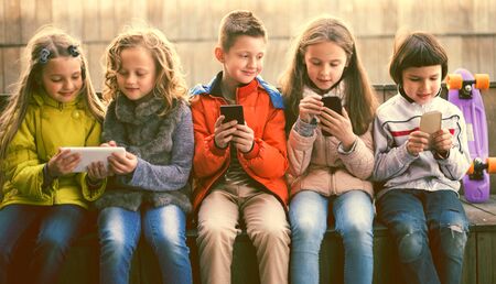 ordinary children playing with the phone on bench outdoorsの写真素材