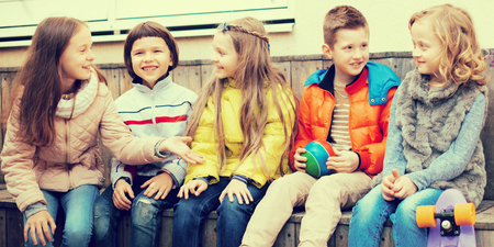 ordinary children communicate sitting on bench in yardの写真素材