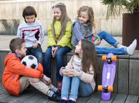 group of ordinary children sitting and communicating on wooden scaffolding schoolyardの写真素材