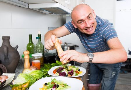 male prepares two salads and fills them with pepper on home kitchenの写真素材