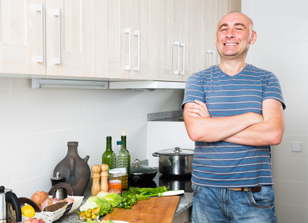 complacent happy man in the prime of life in kitchen prepared two saladsの写真素材