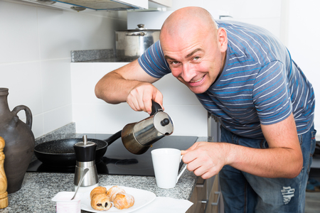 ordinary smiling man preparing coffee in moka pot in the kitchenの写真素材