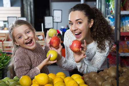 beautiful mother and smiling daughter buying apples in shopの写真素材