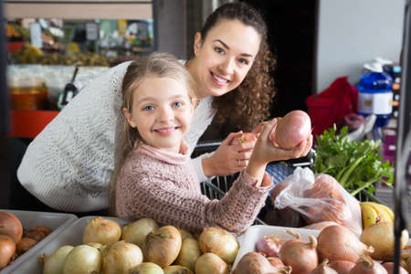 mother and blonde  daughter buying bulb onions in shop. focus on girlの写真素材