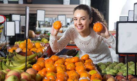 happy young woman buying mandarins in shopの写真素材