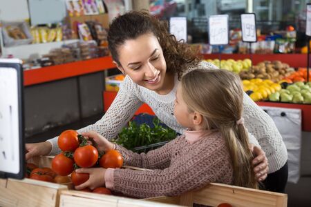 smiling mother and daughter buying tomatoes in shopの写真素材