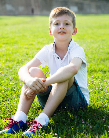 Boy in shirt sitting on the grass in parkの写真素材