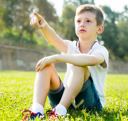 Boy sitting on grass pointing awayの写真素材