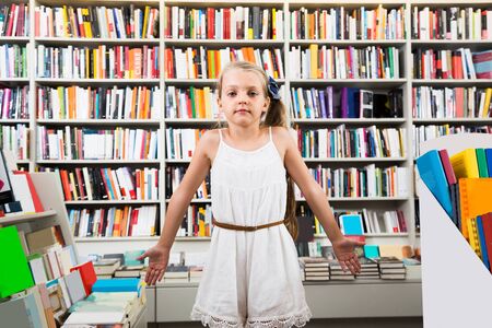 beautiful smart girl child bemused a lot of books in a bookstoreの写真素材