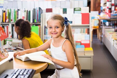 little smiling girl reading a book in a bookstoreの写真素材