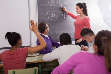 cute student girl solves task near blackboard in multi-ethnic classroom の写真素材