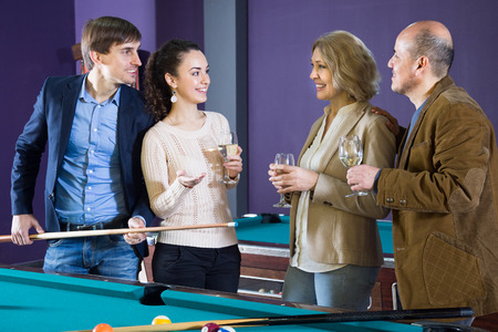 two adult positive couples of different generations talk in the billiard roomの写真素材