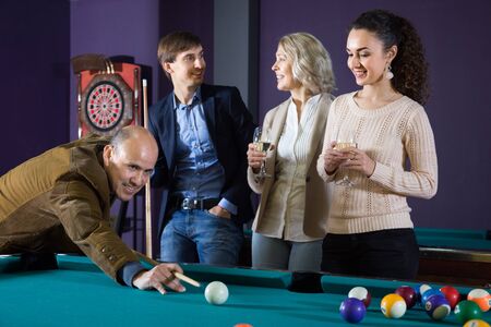 two positive adult couples of different generations talk in the billiard room. focus on mature manの写真素材